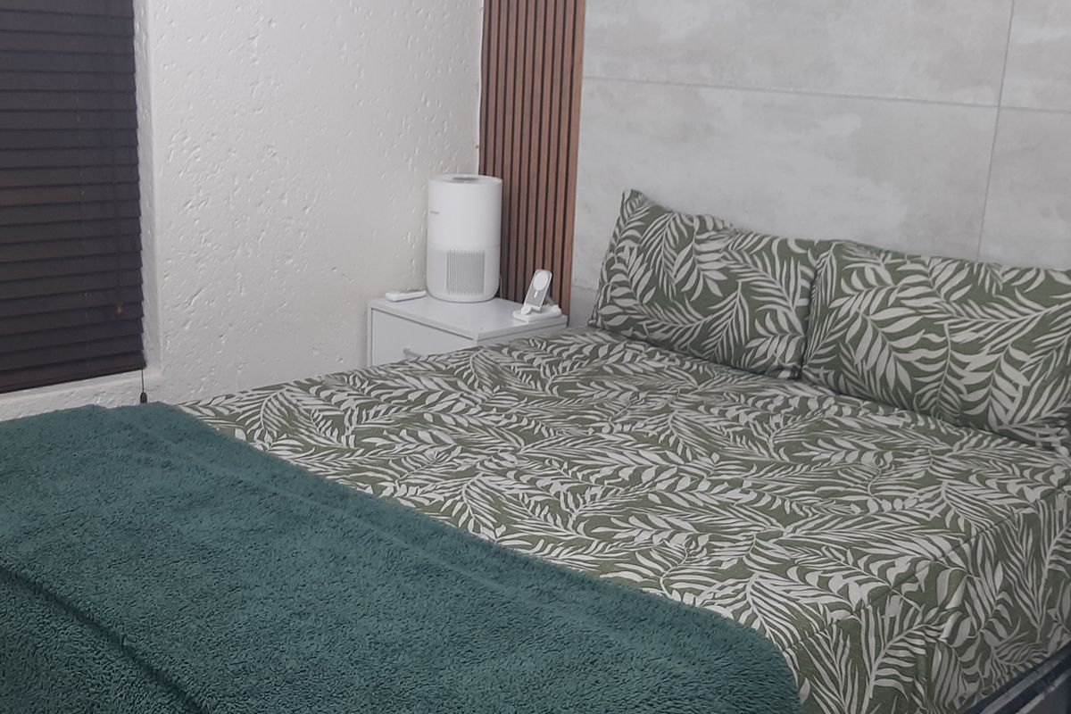 A well-maintained bedroom featuring modern slatted wood wall paneling and large format feature wall tiles, complemented by dark venetian blinds.