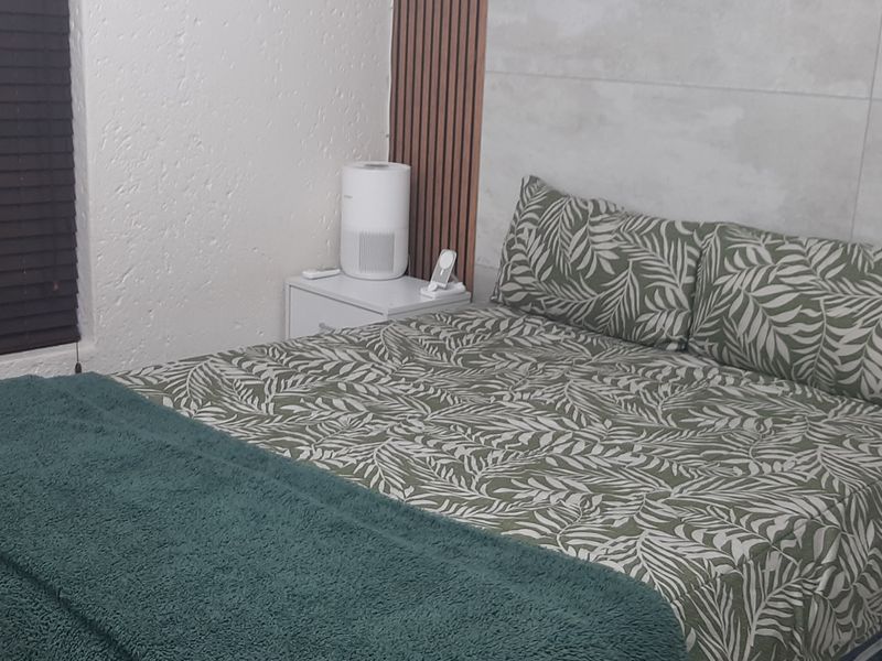 A well-maintained bedroom featuring modern slatted wood wall paneling and large format feature wall tiles, complemented by dark venetian blinds.