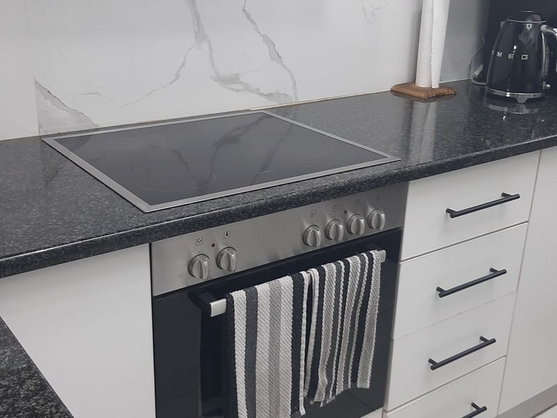 Modern kitchen featuring a sleek granite countertop, integrated induction hob, built-in oven, and elegant marble-look splashback with clean white cabinetry.