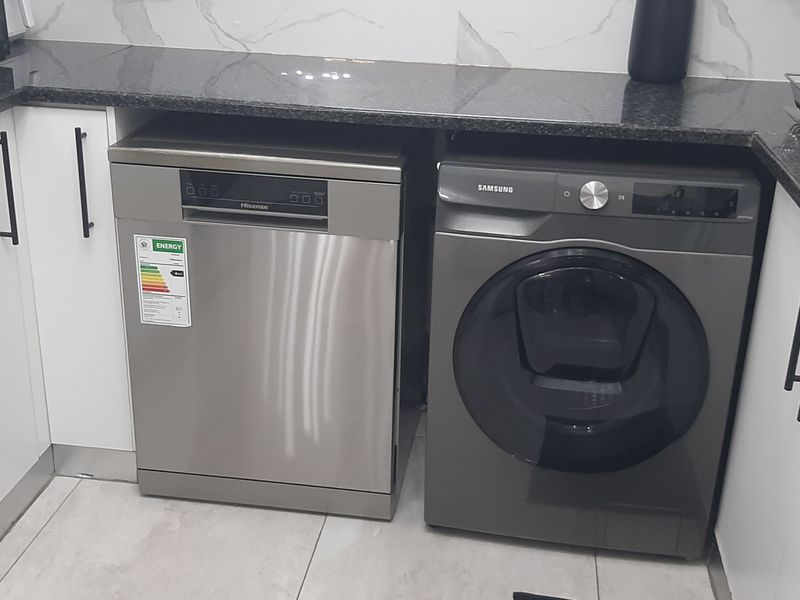 Modern kitchen area featuring granite countertops, marble-look splashback tiling, and integrated space for a dishwasher and washing machine.