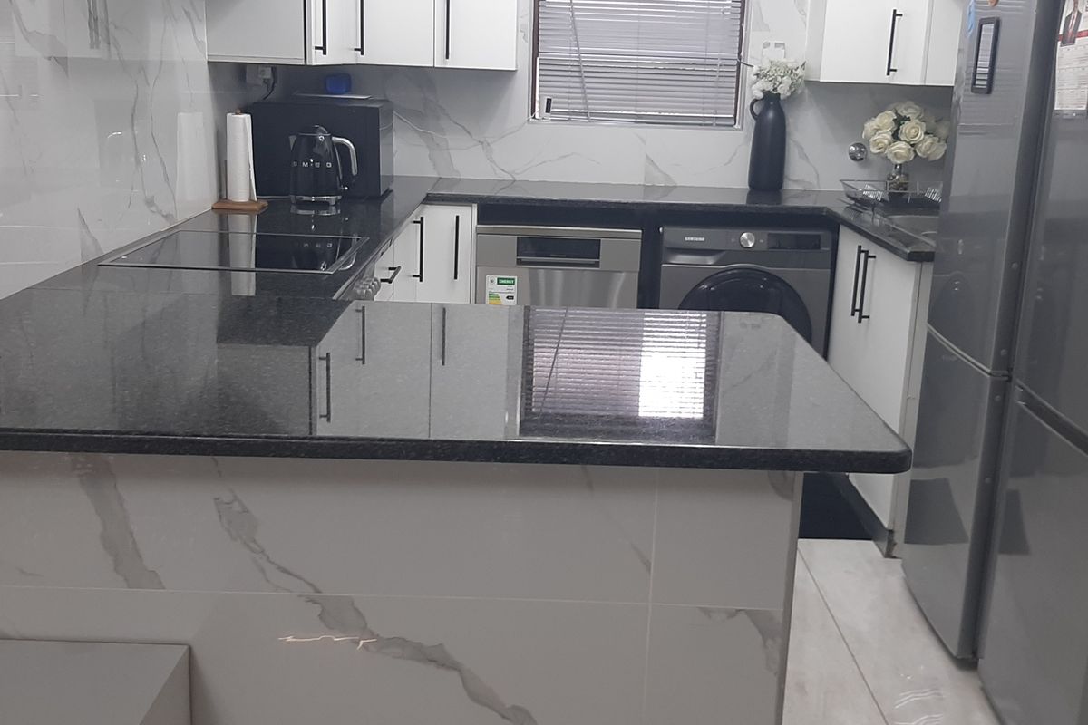 Modern kitchen featuring sleek white cabinetry, contrasting black granite countertops, and elegant marble-look wall tiling with integrated appliance spaces.