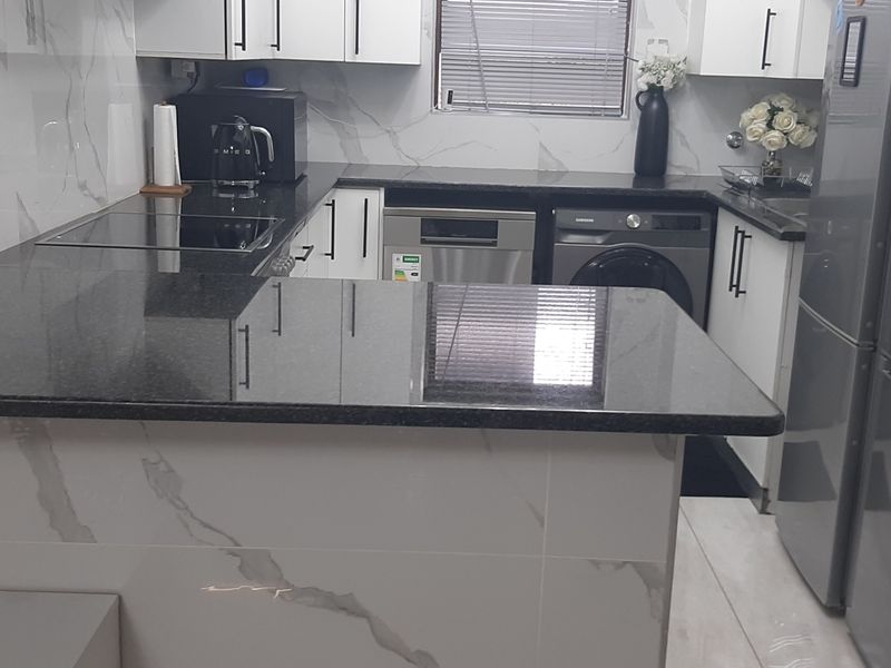 Modern kitchen featuring sleek white cabinetry, contrasting black granite countertops, and elegant marble-look wall tiling with integrated appliance spaces.