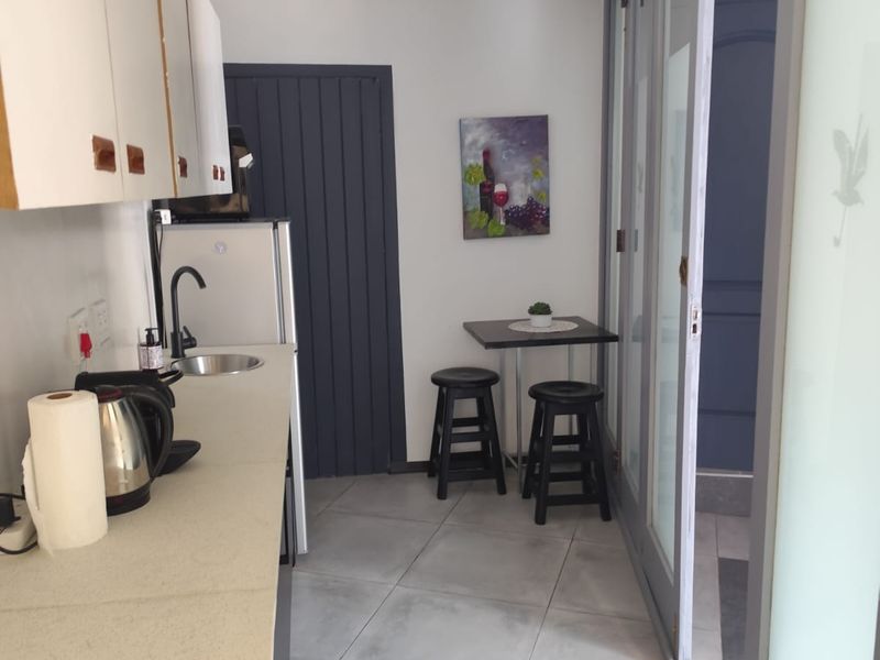 A compact scullery or kitchenette area featuring built-in cabinetry, stone countertops, an undermount sink, and tiled flooring with access via sliding glass doors.