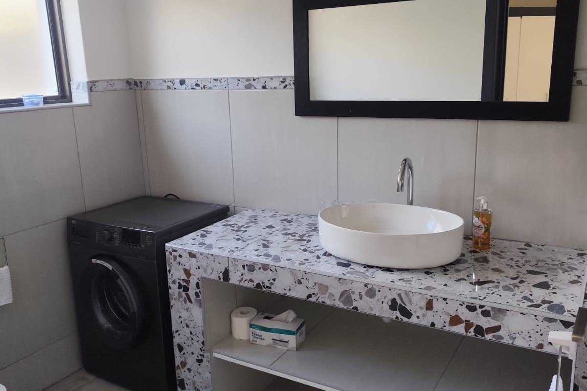 A modern bathroom featuring a custom terrazzo vanity with a vessel sink, chrome faucet, and large wall mirror, complemented by neutral floor and wall tiling.