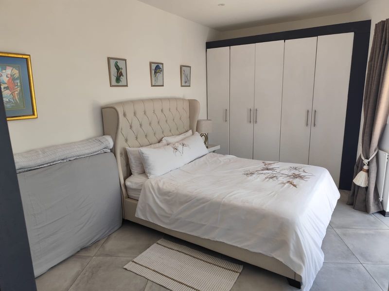 A well-maintained bedroom featuring neutral tiled flooring, recessed ceiling lighting, and ample built-in cupboard storage space.
