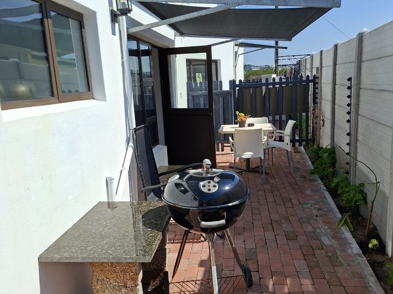A paved outdoor patio area featuring a fixed awning, a built-in stone prep counter, and a secure boundary wall with electric fencing.
