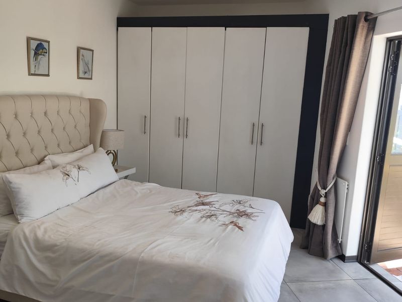 A well-maintained bedroom featuring built-in cupboards, neutral tiled flooring, and direct access to an outdoor area through a sliding door.