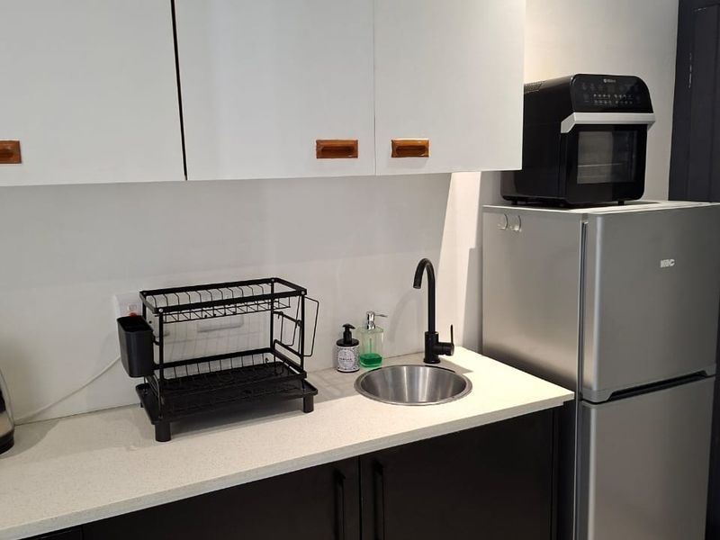 A compact scullery area featuring modern dark lower cabinetry, white upper cabinets, a stone countertop, and a stainless steel sink with a black mixer tap.