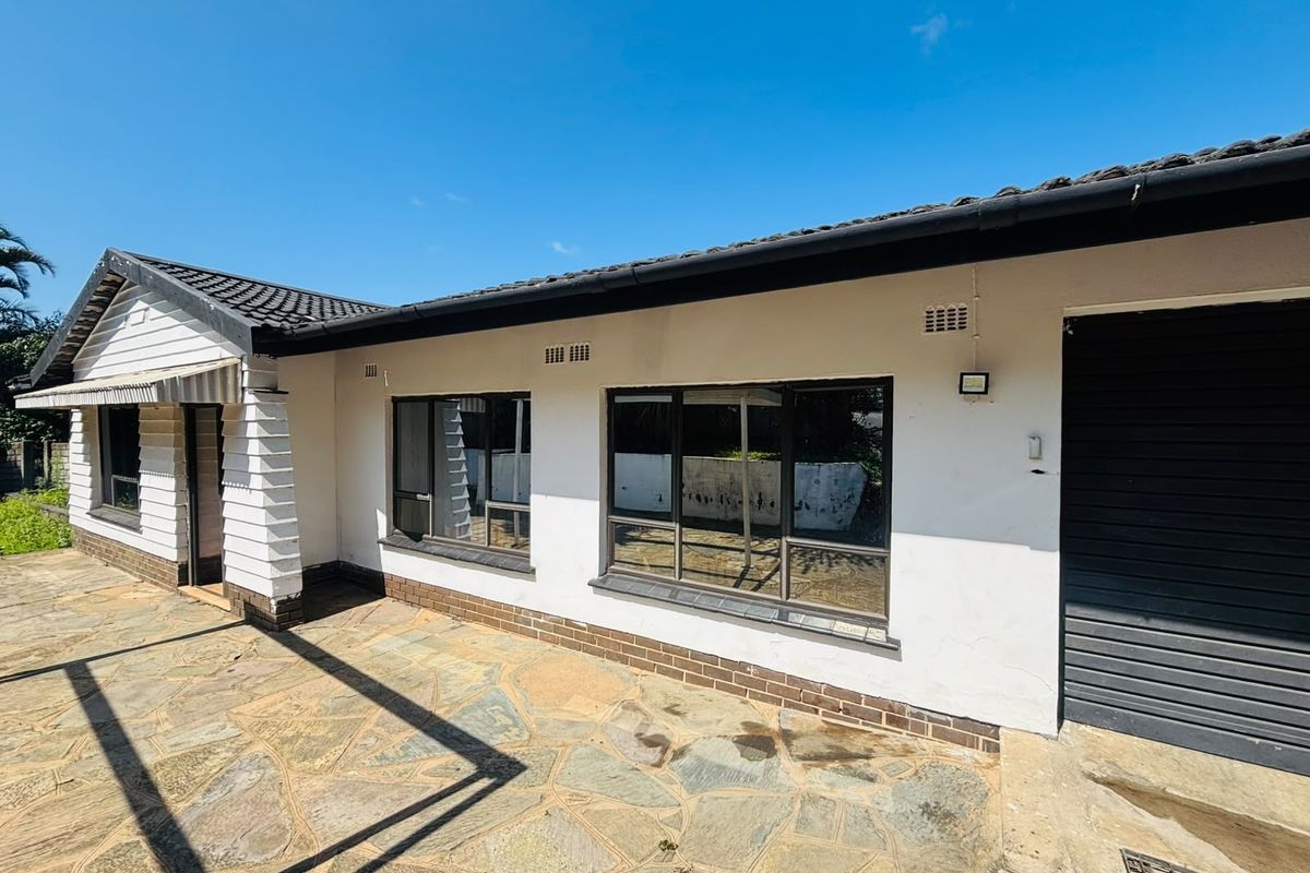 Rear exterior view of the house featuring a stone-paved patio, tiled roof, and aluminium window frames with a garage access point.