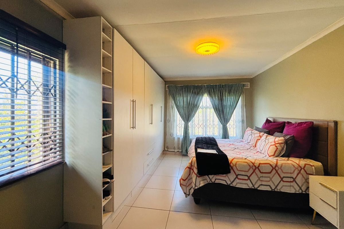 Spacious bedroom featuring extensive built-in cupboards, tiled flooring, and large windows fitted with security bars for added peace of mind.