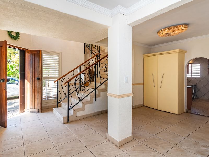 Spacious entrance hall featuring tiled flooring, a decorative wrought iron staircase, and built-in storage, leading through an archway to the kitchen area.