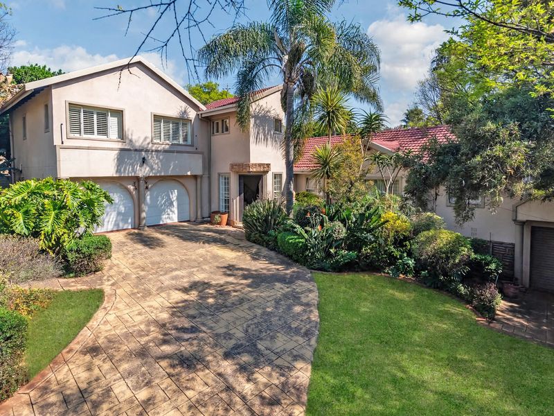 A well-maintained double-story residential property featuring a paved driveway, landscaped front garden, and multiple garage access points.