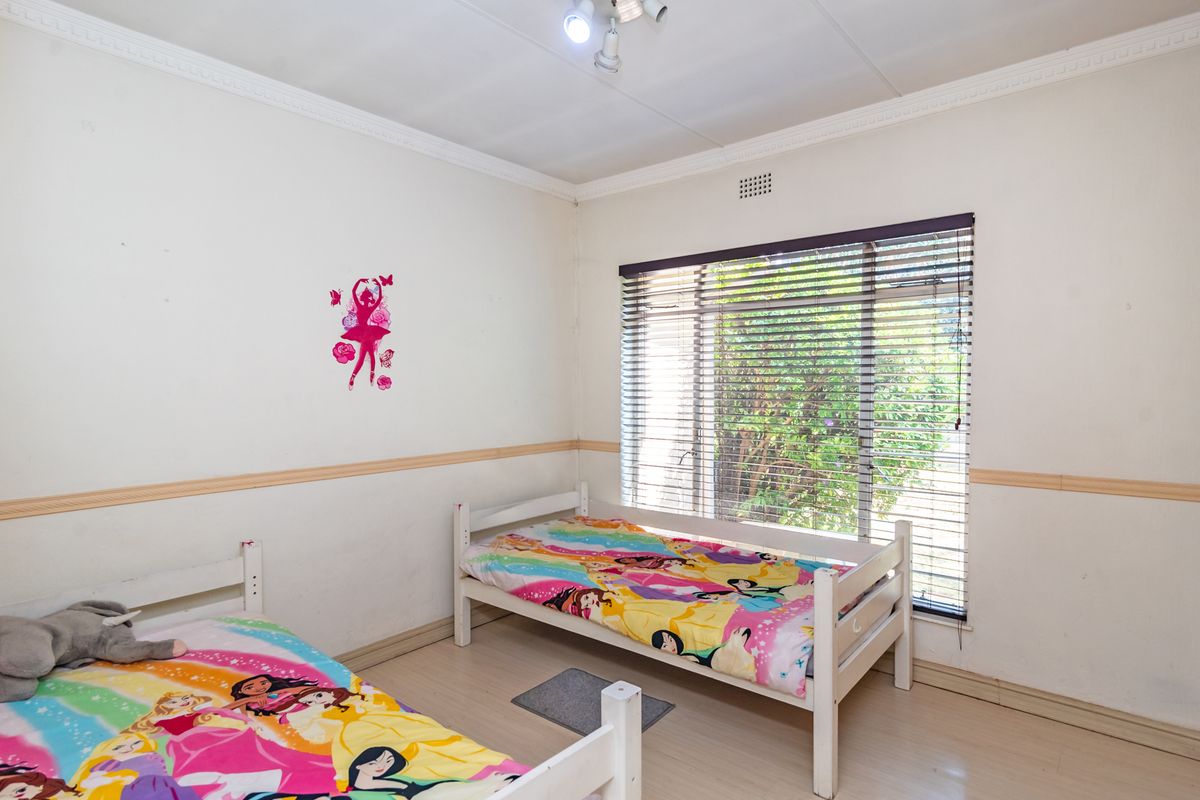 A bedroom featuring laminate flooring, decorative chair rails, ceiling cornicing, and a large window fitted with venetian blinds.