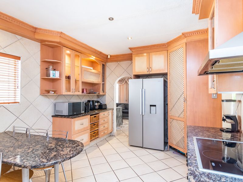 A functional kitchen featuring wooden cabinetry, granite countertops, ceramic tile flooring, and an integrated electric hob with an extractor fan.