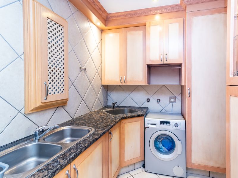 A functional laundry area featuring double and single stainless steel sinks, granite countertops, and ample built-in wooden cabinetry with tiled backsplash.