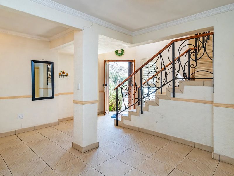 Spacious entrance hall featuring tiled flooring, decorative crown molding, and a wrought iron staircase with a wooden handrail leading to the upper level.