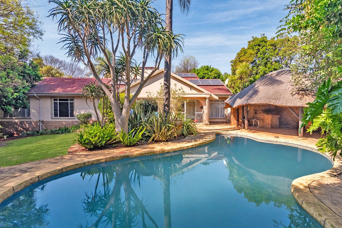 Rear garden view featuring a swimming pool, a thatched lapa entertainment area, and a well-maintained home exterior with solar panels.