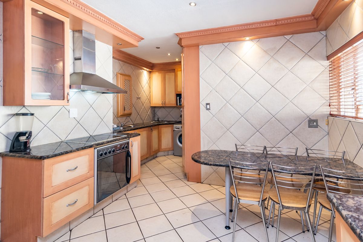 A functional kitchen featuring light wood cabinetry, granite countertops, tiled splashbacks, and integrated appliances, with an adjacent dining area.