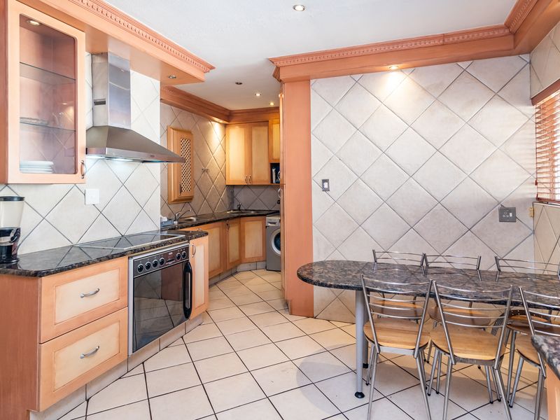 A functional kitchen featuring light wood cabinetry, granite countertops, tiled splashbacks, and integrated appliances, with an adjacent dining area.