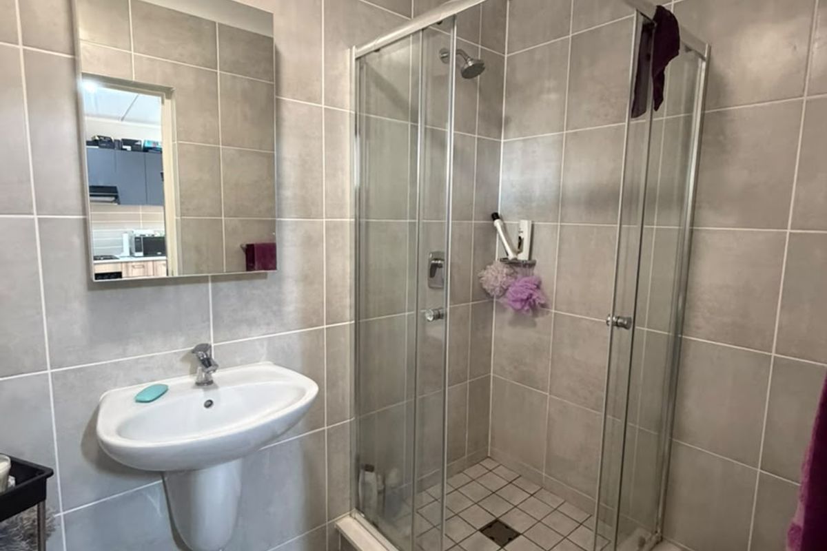 A functional bathroom featuring a glass shower enclosure, pedestal washbasin, and neutral ceramic wall and floor tiling.