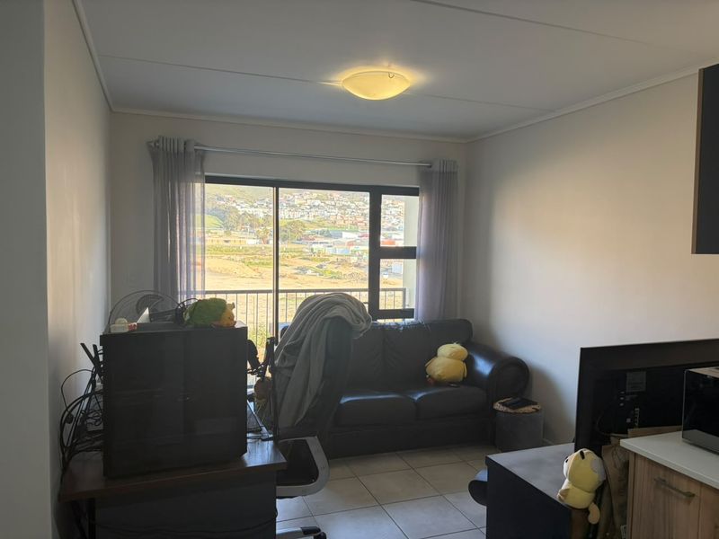 Open plan living area featuring tiled flooring and a large sliding glass door providing natural light and access to a balcony with scenic views.