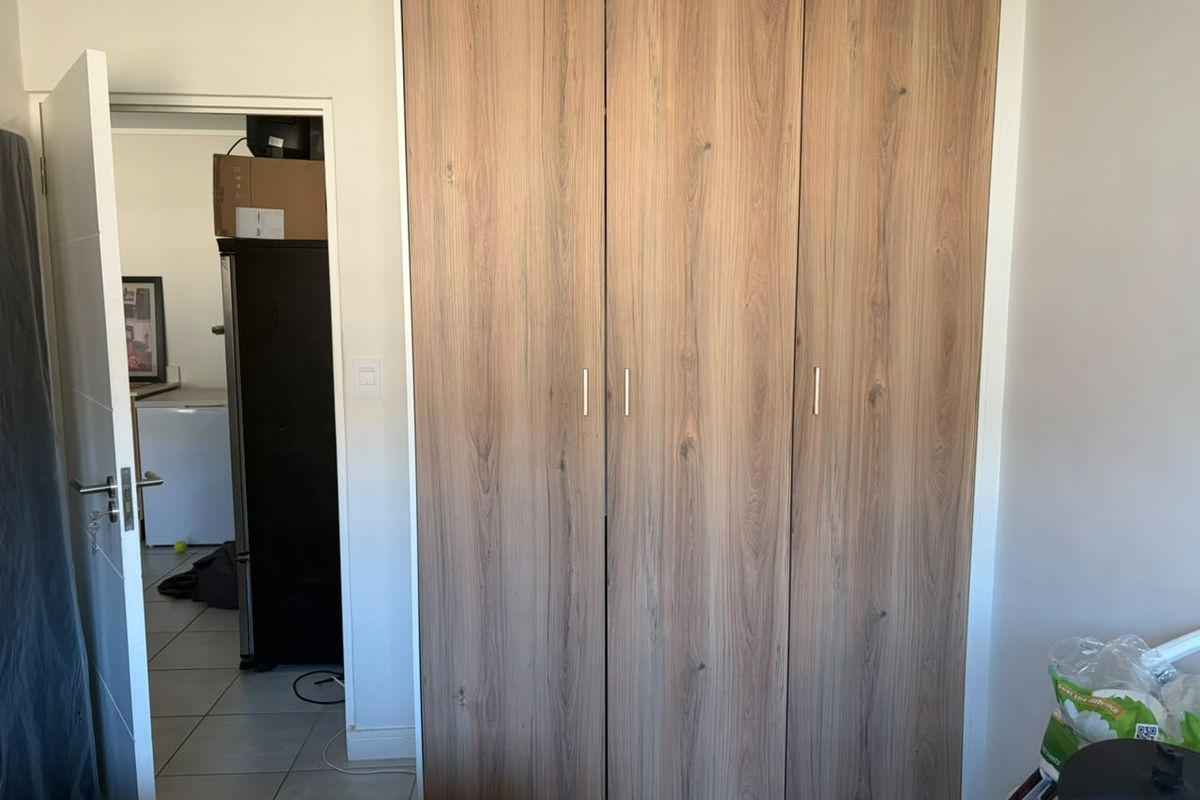 A bedroom featuring a modern wood-grain finish built-in wardrobe with sleek metal handles, providing ample storage space.