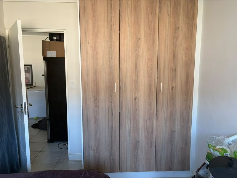A bedroom featuring a modern wood-grain finish built-in wardrobe with sleek metal handles, providing ample storage space.