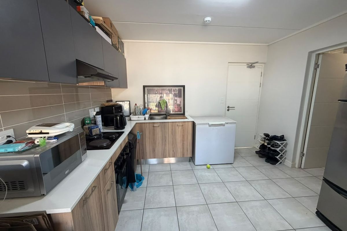 A functional kitchen featuring modern wood-finish cabinetry, dark overhead cupboards, a tiled backsplash, and a built-in hob with an extractor fan.
