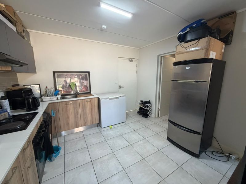 A functional kitchen featuring wood-finish cabinetry, tiled flooring, and integrated cooking appliances, providing a practical workspace with direct access to adjacent areas.