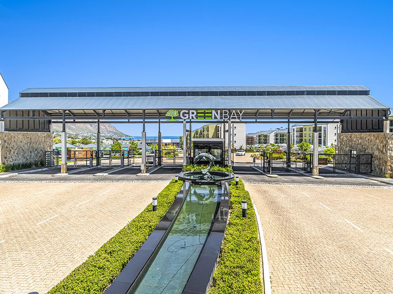 The main entrance and security gatehouse of the Greenbay apartment complex, featuring a landscaped water feature and paved driveway access.