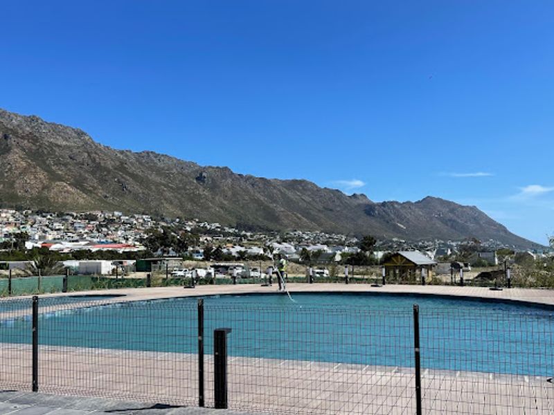 A communal swimming pool area featuring a paved deck, safety fencing, and scenic mountain views in the background.