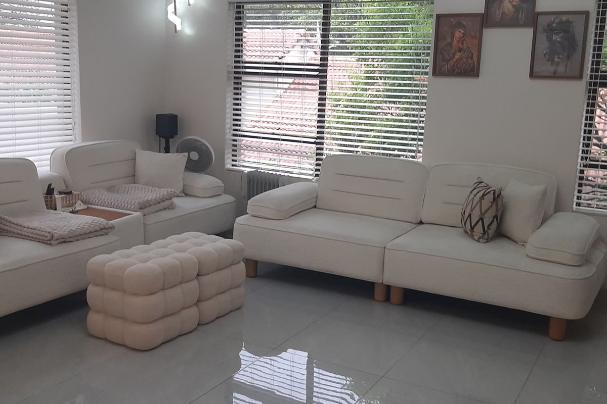 A bright and well-maintained living room featuring large windows with venetian blinds and polished tiled flooring.