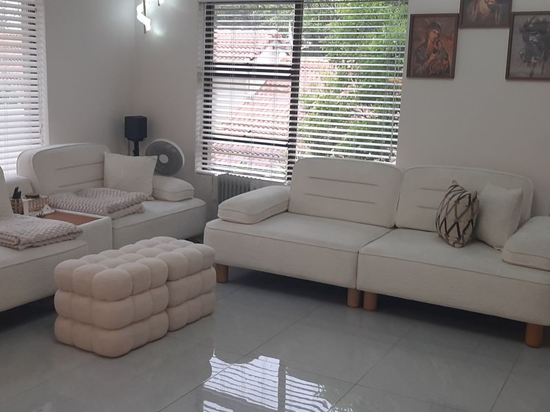 A bright and well-maintained living room featuring large windows with venetian blinds and polished tiled flooring.