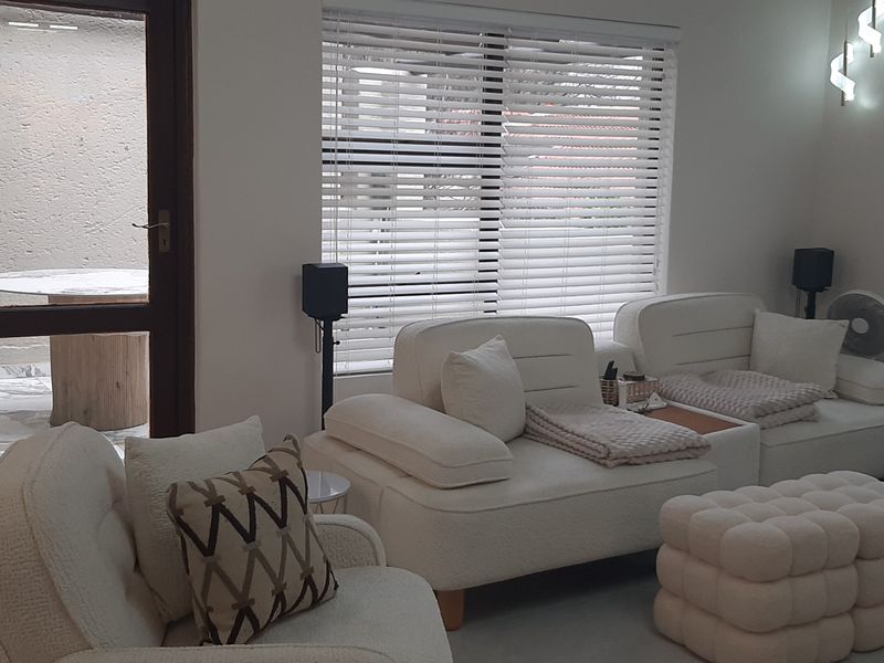 A bright living room featuring tiled flooring, modern wall lighting, and venetian blinds, with direct access to an outdoor patio area.