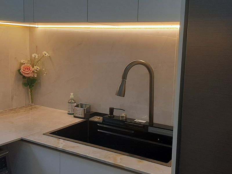 Modern kitchen area featuring a sleek stone countertop, marble-look backsplash, undermount sink with a gooseneck faucet, and integrated under-cabinet LED lighting.