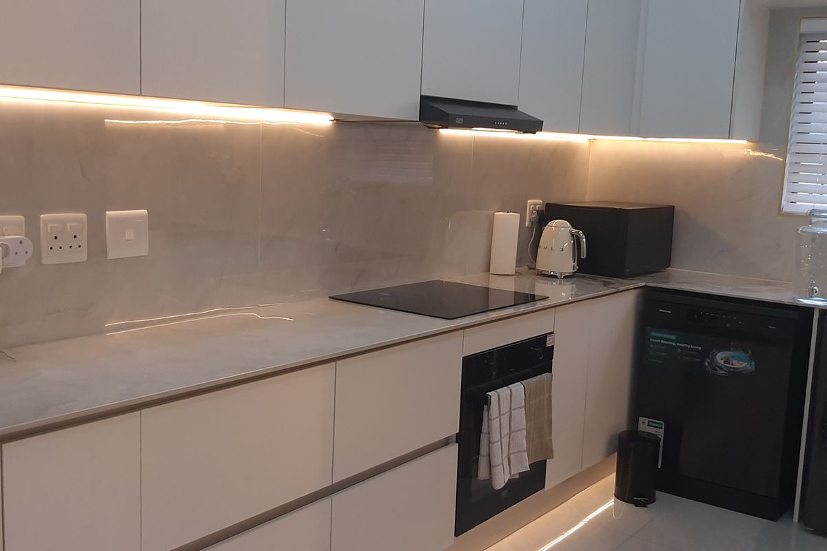 Modern kitchen featuring sleek handleless cabinetry, stone countertops, integrated hob and oven, and ambient under-cabinet LED lighting.