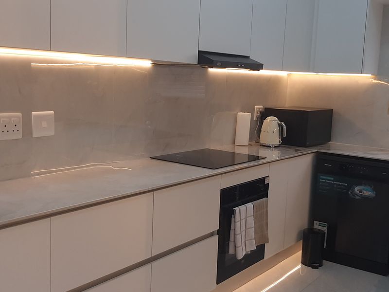 Modern kitchen featuring sleek handleless cabinetry, stone countertops, integrated hob and oven, and ambient under-cabinet LED lighting.