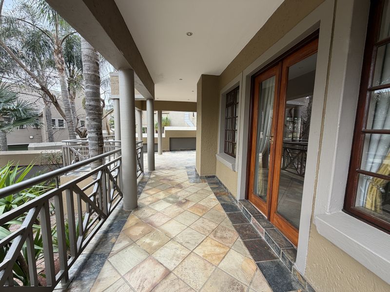 A covered balcony featuring tiled flooring, metal balustrades, and wooden framed glass doors providing access to the interior living space.