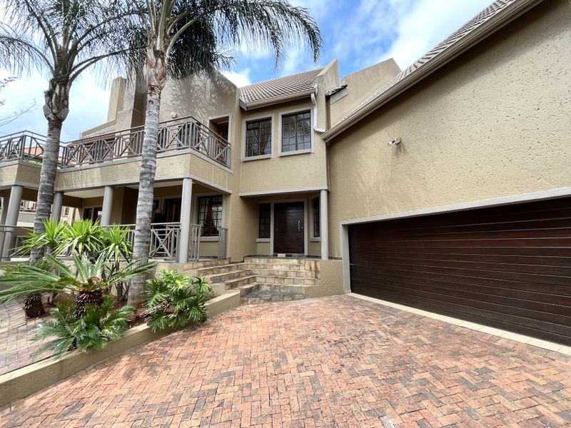 Front elevation of a cluster home featuring a paved driveway, double garage, stone-clad entrance steps, and an upper-level balcony with metal railings.