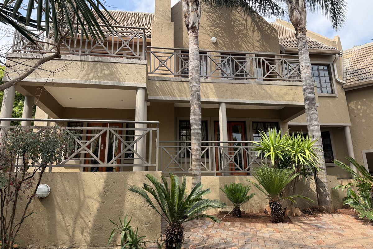 Rear elevation of a double-story cluster home featuring a covered patio, upper balcony with metal railings, and a paved garden area.
