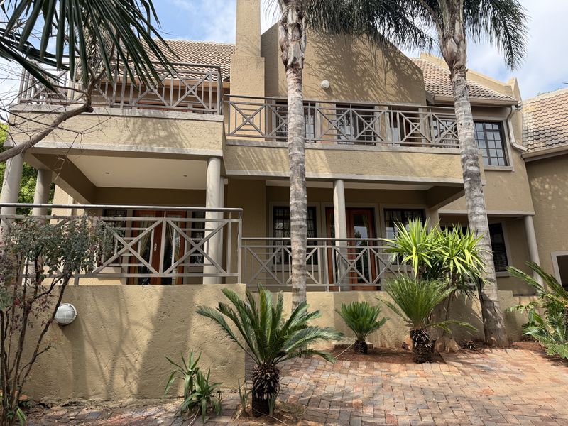 Rear elevation of a double-story cluster home featuring a covered patio, upper balcony with metal railings, and a paved garden area.