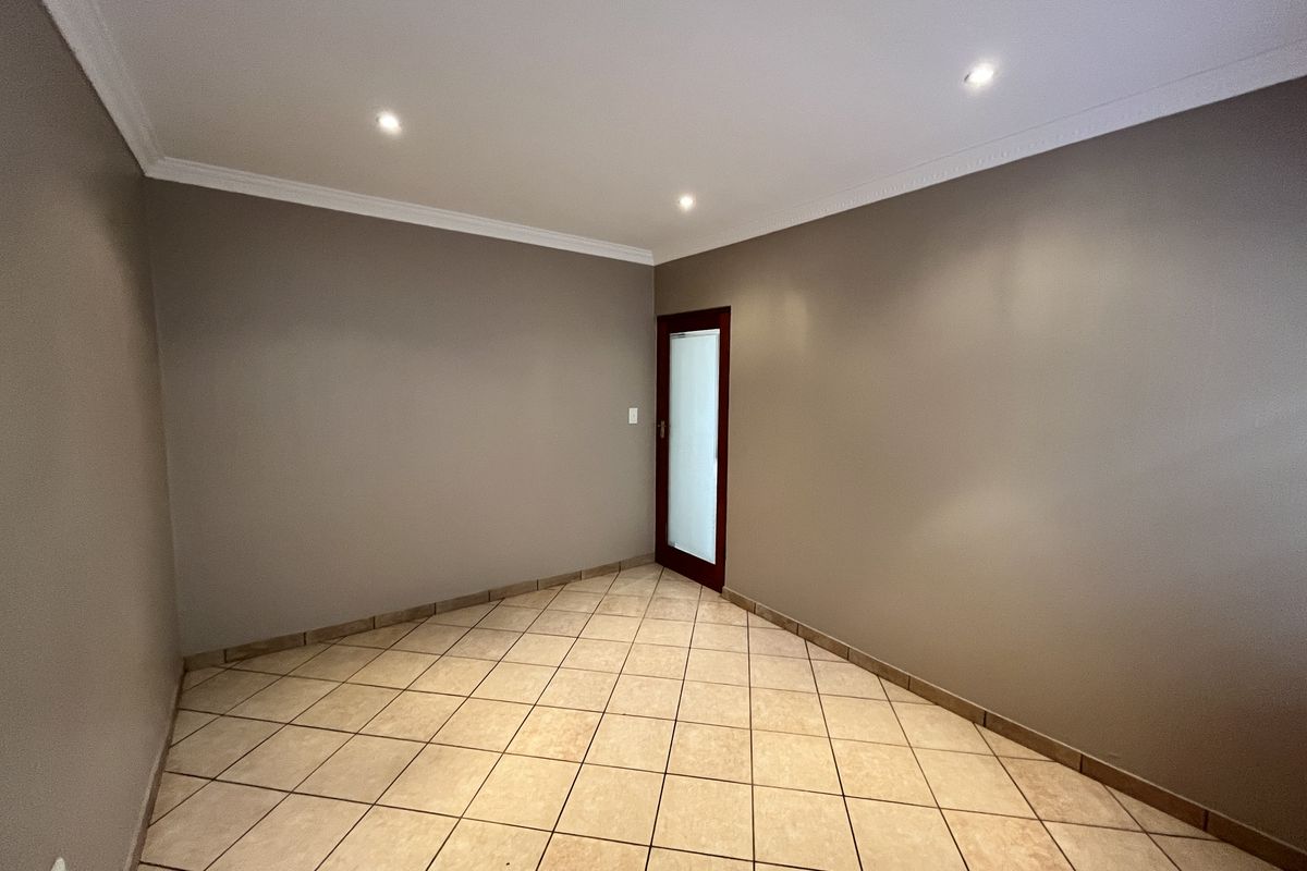 A clean, empty living space featuring neutral wall tones, tiled flooring, recessed downlighting, and a modern frosted glass door.