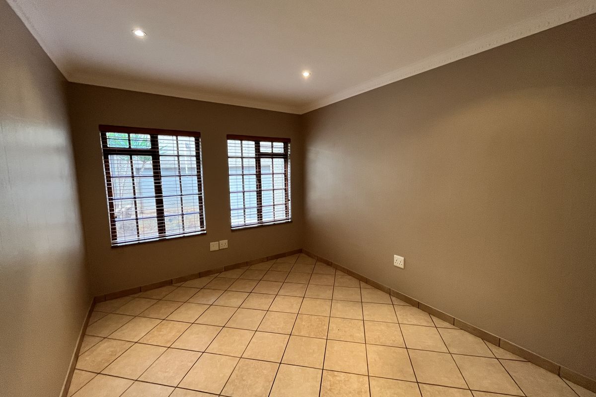 A clean, empty bedroom featuring neutral wall tones, tiled flooring, recessed downlighting, and coved cornicing, offering a versatile space ready for personalization.