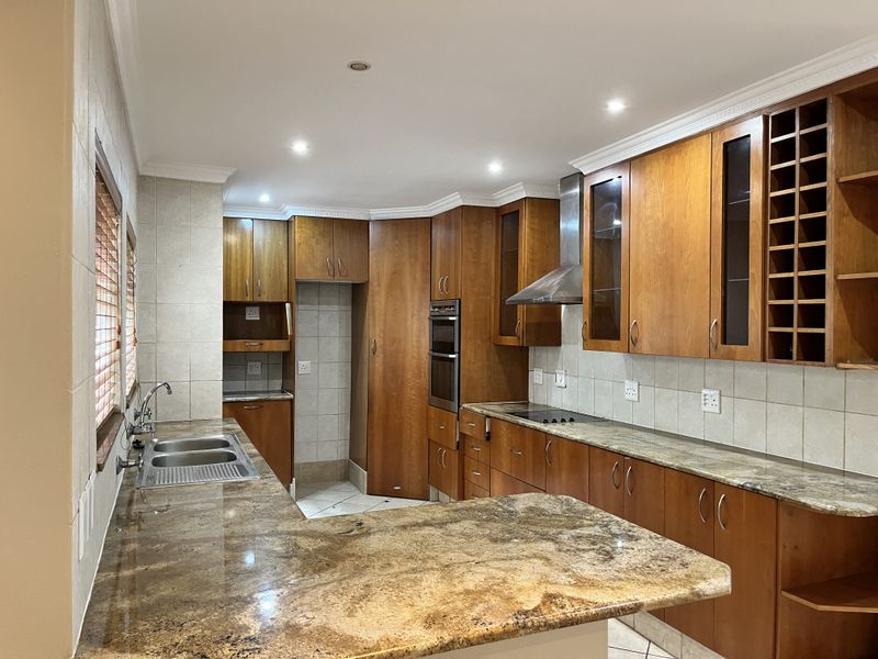 Spacious kitchen featuring warm wooden cabinetry, granite countertops, built-in oven, electric hob, and ample storage including a dedicated wine rack.