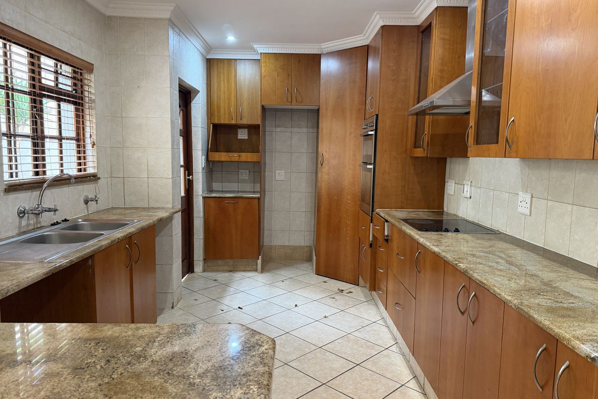 A spacious kitchen featuring wooden cabinetry, granite countertops, built-in oven, electric hob, and tiled finishes throughout.