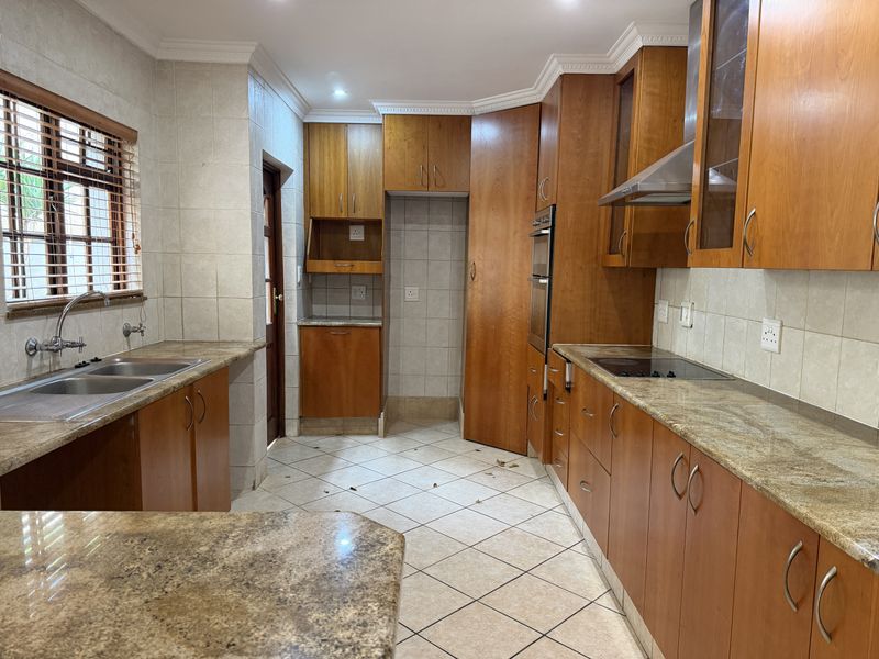 A spacious kitchen featuring wooden cabinetry, granite countertops, built-in oven, electric hob, and tiled finishes throughout.