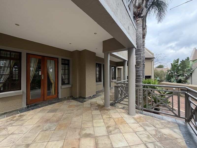 A spacious covered patio featuring tiled flooring, structural columns, and a metal balustrade, providing a functional outdoor entertainment area.