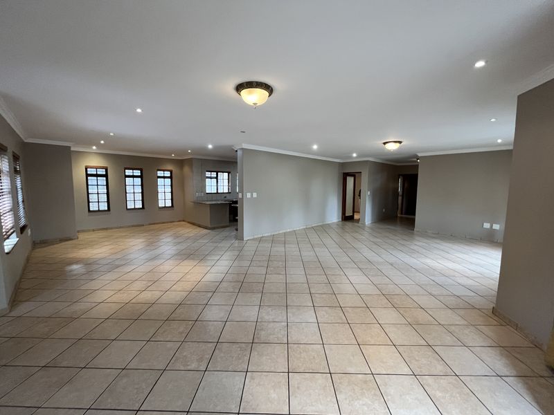 Spacious open-plan living area featuring neutral tiled flooring, recessed lighting, and a breakfast counter, offering a versatile layout for dining and lounge arrangements.
