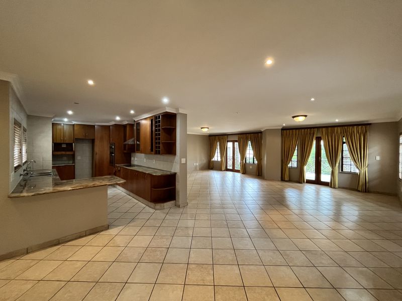 Spacious open-plan living and kitchen area featuring tiled flooring, built-in wooden cabinetry, granite countertops, and multiple sets of french doors leading outdoors.