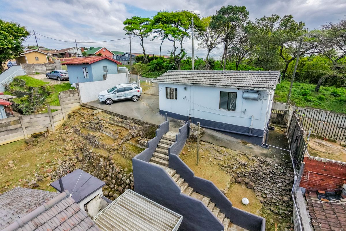 Aerial view of the property exterior, showcasing the building structure, concrete staircase, driveway, and surrounding terraced landscape.